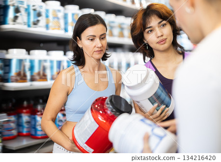 Young guy and women choosing protein powder jar in sports nutrition store 134216420