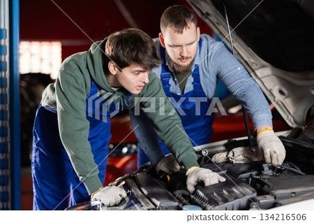 Two auto mechanics work together to diagnose an engine under the hood of a car in repair shop 134216506