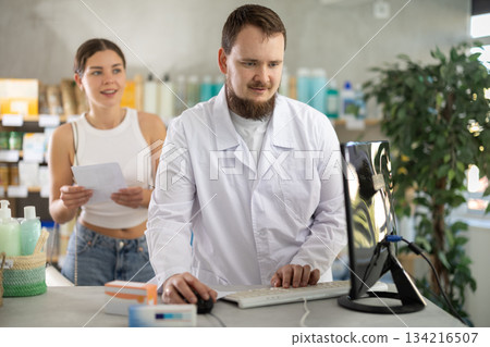 Male pharmacist helps female customer find prescription medication 134216507