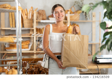 Young woman with baguette in bag in bakery 134216509