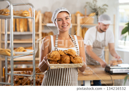 Young saleswoman displays croissants in square wicker basket 134216532