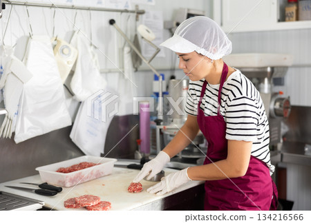 Workwoman pressing raw ground beef hamburger patties in butcher shop 134216566