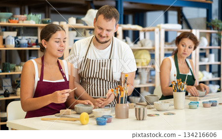 Pupils are sitting near work table, sculpting plate of raw clay under supervision of male teacher 134216606