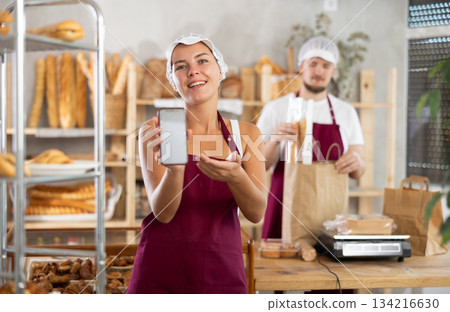 Young saleswoman displays a mobile application in bakery shop 134216630