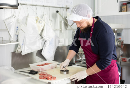Bearded worker pressing ground beef hamburger patties in butcher shop Bearded worker pressing ground beef hamburger patties in butcher shop 134216642