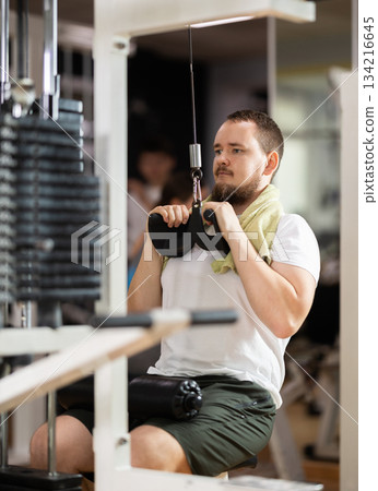 Man in gym performs exercises for arm muscles using cable crossover machine and pull weighted rope Man in gym performs exercises for arm muscles using cable crossover machine and pull weighted rope 134216645