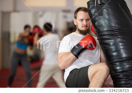 Bearded man punches and kicks punching bag in gym. 134216723