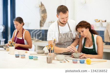 Pupils are sitting near work table, sculpting plate of raw clay under supervision of male teacher Pupils are sitting near work table, sculpting plate of raw clay under supervision of male teacher 134216852