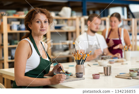 During workshop at master class, female employee paints clay vessel plate During workshop at master class, female employee paints clay vessel plate 134216855