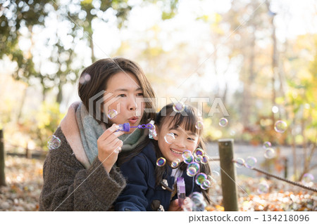 秋日的公園裡，父母和孩子們在玩泡泡。一位年長的母親和她可愛的女兒。 134218096