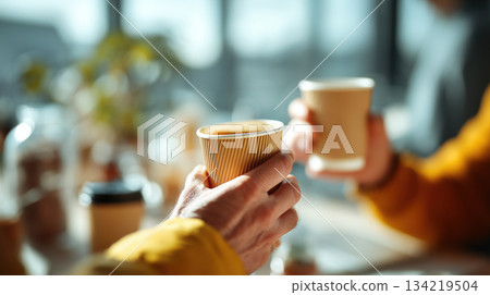 Two people holding coffee cups in bright setting 134219504