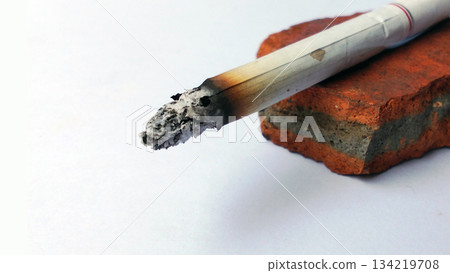 Close-Up of a Burning Cigarette with Ash on a Brick Surface 134219708