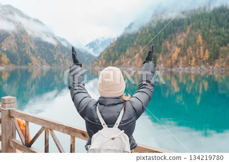 Happy woman traveler travel in jiuzhaigou national park in Sichuan, China. Tourist sightseeing Long lake and snow mountain in Autumn season. Famous Landmark and Vacation near Chengdu, China Happy woman traveler travel in jiuzhaigou national park in Sichuan, China. Tourist sightseeing Long lake and snow mountain in Autumn season. Famous Landmark and Vacation near Chengdu, China 134219780