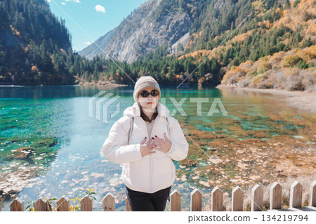 Happy woman traveler travel in jiuzhaigou national park in Sichuan, China. Tourist sightseeing Five Flower lake and snow mountain in Autumn season. Famous Landmark and Vacation near Chengdu, China Happy woman traveler travel in jiuzhaigou national park in Sichuan, China. Tourist sightseeing Five Flower lake and snow mountain in Autumn season. Famous Landmark and Vacation near Chengdu, China 134219794