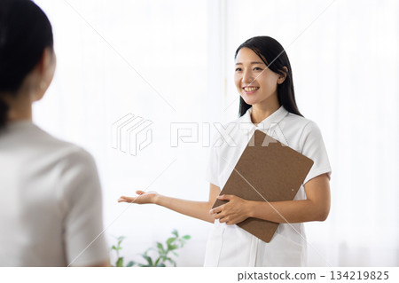 一位身穿白大褂的女士手持醫療問卷，正在指導一位病人。 134219825