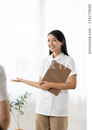 A woman in a white coat holding a medical questionnaire and guiding a patient 134219826