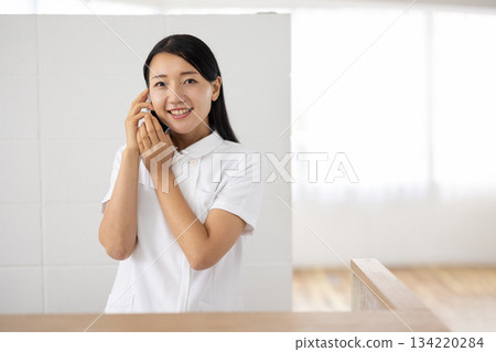 A woman in a white coat holding a smartphone to her ear A woman in a white coat holding a smartphone to her ear 134220284