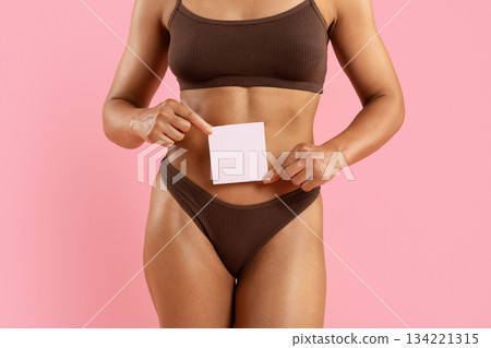 Young black woman in underwear holding blank paper sheet near her stomach Young black woman in underwear holding blank paper sheet near her stomach 134221315