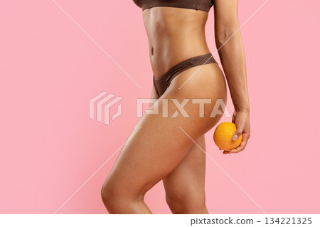 No Cellulite. Young black woman holding an orange beside her thigh in brown underwear No Cellulite. Young black woman holding an orange beside her thigh in brown underwear 134221325