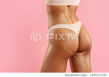 Lower body of young black woman in beige underwear on pink background Lower body of young black woman in beige underwear on pink background 134221330