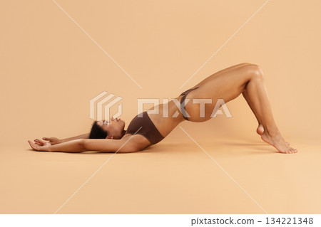 Young black woman performing bridge pose on beige studio background Young black woman performing bridge pose on beige studio background 134221348