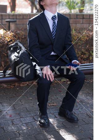 A male businessman sitting on a bench during an outside sales call and worrying. No face. A male businessman sitting on a bench during an outside sales call and worrying. No face. 134222270