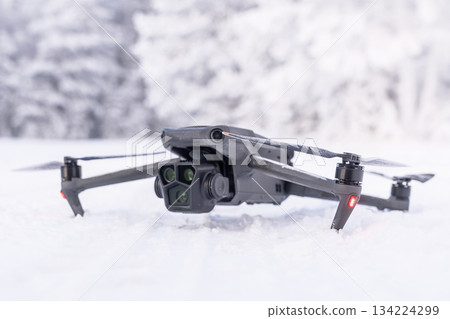 A black drone on the background of a winter forest. Winter aerial photography and aerial photography from drones while traveling. Features of quadcopter operation in the cold season. A black drone on 134224299