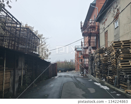 Urban alleyway with pallets, fire escape, and cloudy sky 134224863