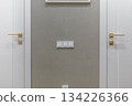 Symmetrical White Doors with Golden Handles and Light Switches in Modern Interior 134226366