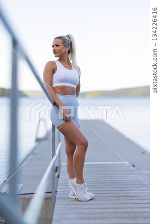 Woman resting after outdoor fitness on a dock with scenic water views Woman resting after outdoor fitness on a dock with scenic water views 134226416
