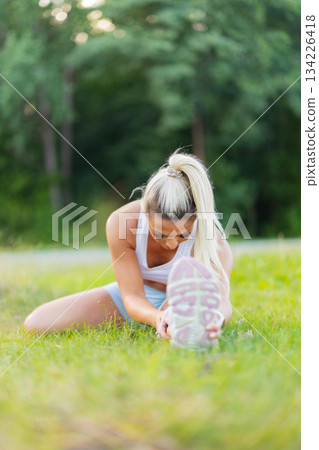Young woman stretching outdoors in a park setting during a morning workout 134226418