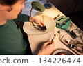 Man renewing vintage electric lamp at workshop, disassembling light bulb socket with screwdriver. 134226474