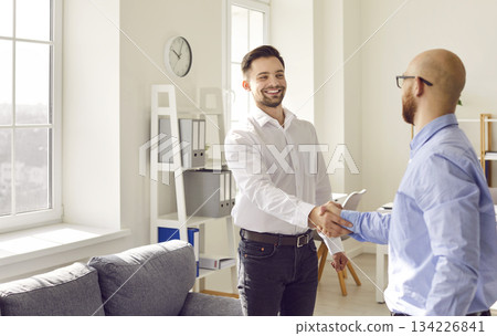 Two business men standing in office making deal shaking hands celebrating business achievement. 134226841