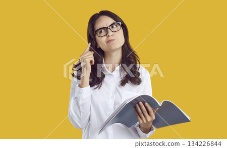 Puzzled brunette woman student in glasses thinking looking up with pen and copybook in hands. Puzzled brunette woman student in glasses thinking looking up with pen and copybook in hands. 134226844
