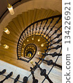 Spiral staircase viewed from above with ornate railing and warm hanging lights 134226921