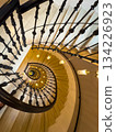Spiral staircase viewed from above with ornate iron railing and warm hanging lights 134226923