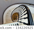 Spiral staircase viewed from above with ornate black railing and warm lighting in circular stairwell 134226925