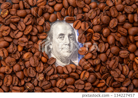 roasted coffee beans surrounding a U.S. $100 bill with Benjamin Franklin 134227457