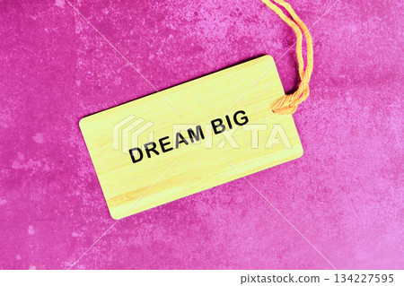 A tag with the inscription DREAM BIG sits on a textured purple surface, with a yellow string adding a subtle accent. It encourages vision and aspirations 134227595