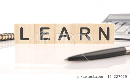Wooden blocks spelling LEARN rest on a white surface near a pen, notebook, and calculator, suggesting educational pursuits and growth 134227619