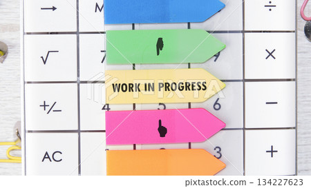 A calculator features colorful sticky notes, including one boldly displaying Work In Progress, alongside mathematical symbols. This close-up captures a focused, process-oriented scene A calculator features colorful sticky notes, including one boldly displaying Work In Progress, alongside mathematical symbols. This close-up captures a focused, process-oriented scene 134227623