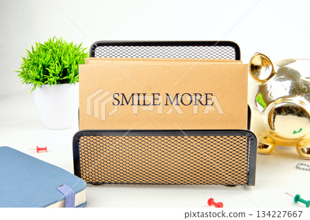 A charming desk setup features a message that reads smile more, accompanied by greenery, a piggy bank, and colorful stationery items that inspire positivity and happiness 134227667