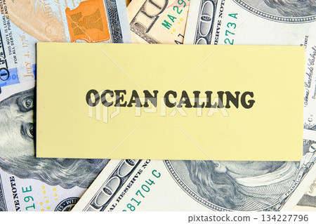 A warm note with the words Ocean Calling rests atop scattered dollar bills, symbolizing a desire for adventure and the journey to coastal destinations filled with beauty 134227796