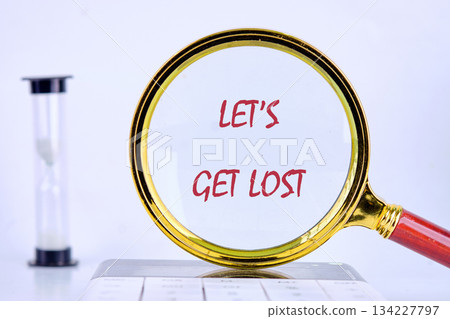A magnifying glass focusing on the phrase Lets Get Lost invites adventure and exploration. Behind it, an hourglass symbolizes the fleeting nature of time, urging spontaneity 134227797