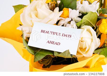 A stunning array of fresh flowers in vibrant yellow paper, featuring white roses and cheerful yellow blooms. A card with an encouraging note hints at joyous moments to come A stunning array of fresh flowers in vibrant yellow paper, featuring white roses and cheerful yellow blooms. A card with an encouraging note hints at joyous moments to come 134227808