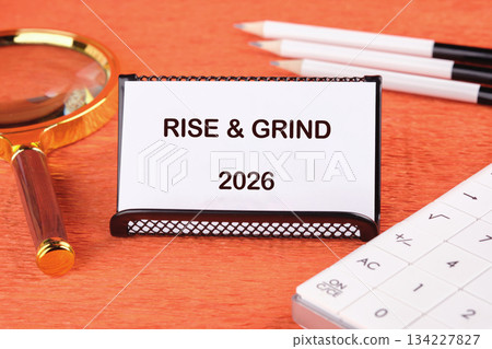 A bright workspace features a sign that reads Rise Grind 2026, symbolizing dedication and hard work. Nearby tools like a magnifying glass and keyboard enhance the productivity theme 134227827