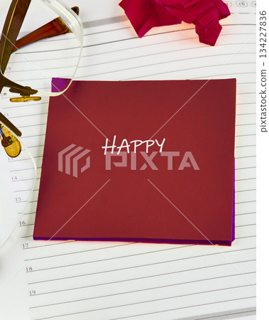 A bright red note with the word happy is nestled on a lined notebook, surrounded by stylish glasses and a vibrant rose, creating an uplifting atmosphere A bright red note with the word happy is nestled on a lined notebook, surrounded by stylish glasses and a vibrant rose, creating an uplifting atmosphere 134227836