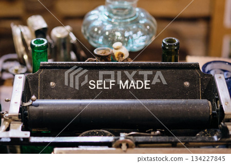 In a cozy workshop, a vintage typewriter captures the essence of self-made creativity. Surrounded by unique glass bottles, it inspires artistic expression and nostalgia for simpler times 134227845