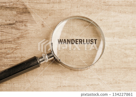 Magnifying glass highlights the word wanderlust, resting on a rustic wooden table. This scene evokes a sense of adventure and curiosity about travel and exploration 134227861