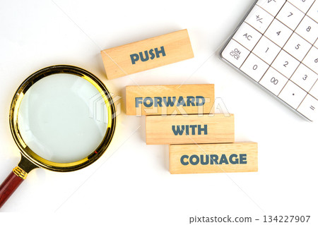 Wooden blocks spell out a motivational phrase encouraging bravery and determination. A magnifying glass adds a subtle touch to a bright, inviting workspace, inspiring creativity and focus Wooden blocks spell out a motivational phrase encouraging bravery and determination. A magnifying glass adds a subtle touch to a bright, inviting workspace, inspiring creativity and focus 134227907